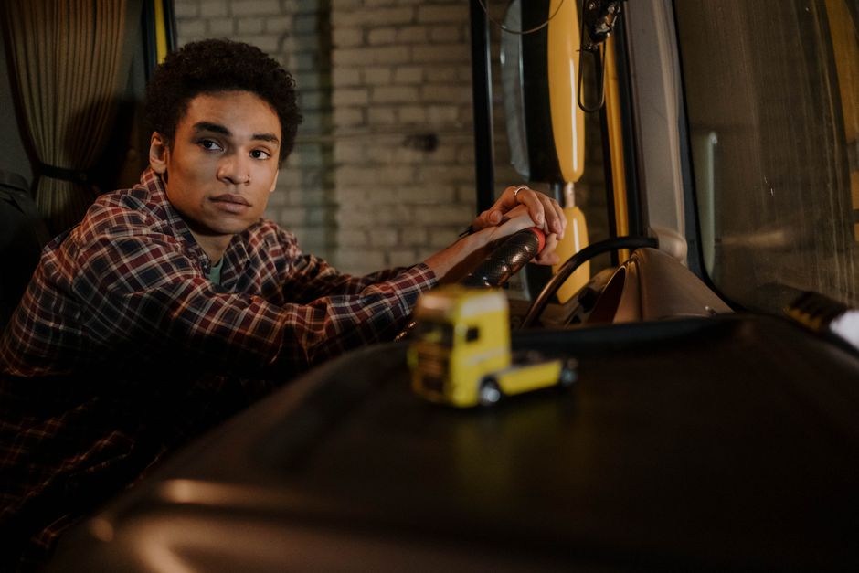 Een bus- en vrachtwagenchauffeur tijdens zijn opleiding met een vrachtwagen en bus in de achtergrond.
